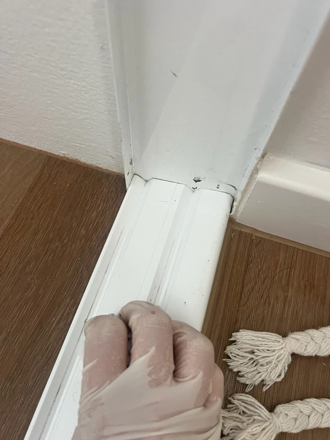 A gloved hand detail-cleaning skirting boards and door frames
